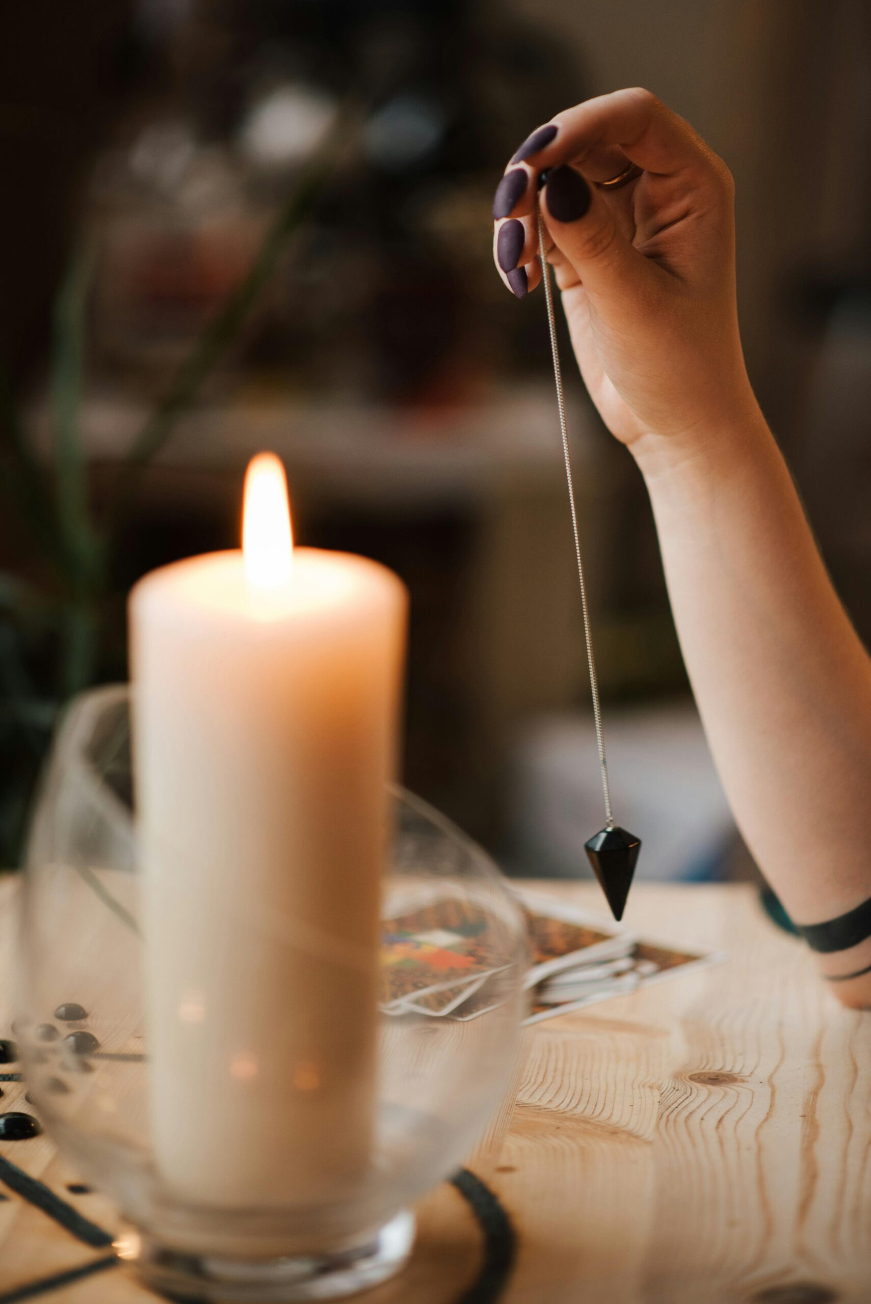 A hand holds a pendulum over tarot cards by candlelight, evoking a mystical ambiance.